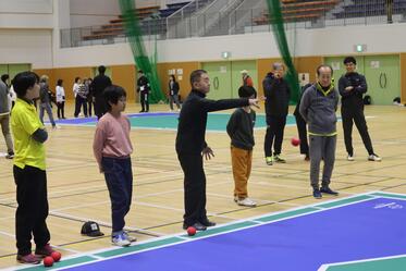 選手がボッチャボールを投げているのをその他の選手が見ている写真
