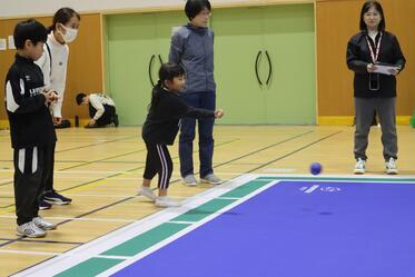 子ども手がボッチャボールを投げている写真